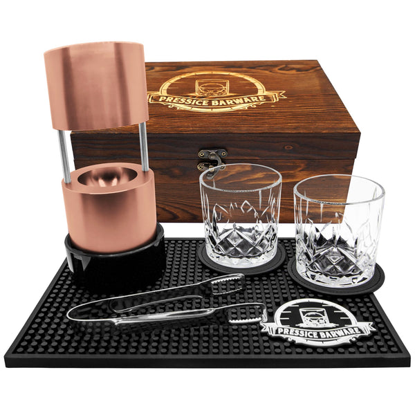 Barware set with copper elements, glasses, and tools on a branded mat and wooden box.